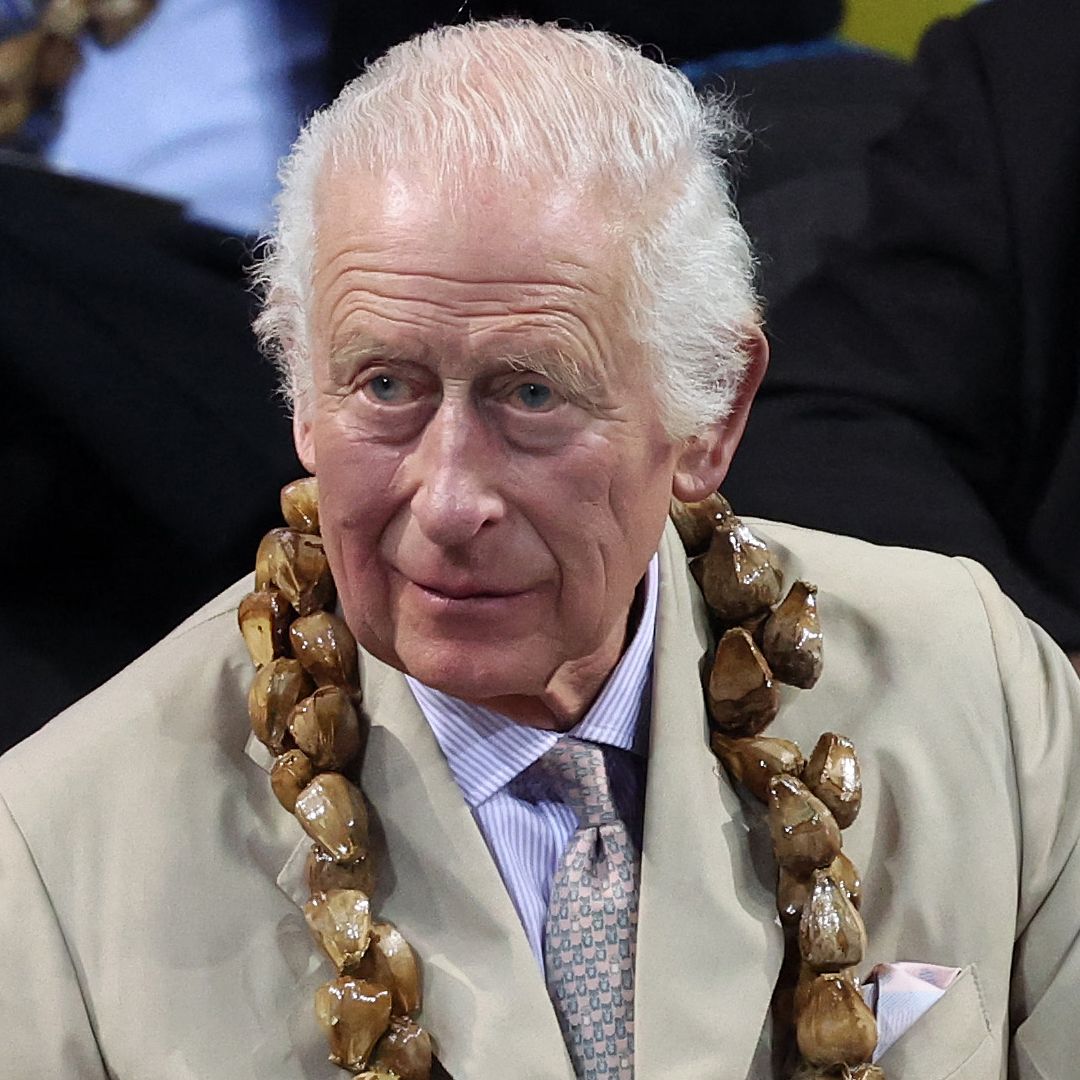 King Charles wears a light linen suit with a purple tie and white suit while looking sombre