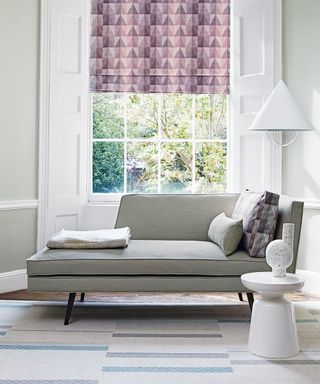 Contemporary living room picture with gray couch and purple geometric patterned blinds and cushion.