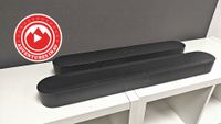 Sonos Beam Ultra and Sonos Beam Gen 2 on a white table. There is also a red roundel on the top left corner saying 'Adventures in AV'
