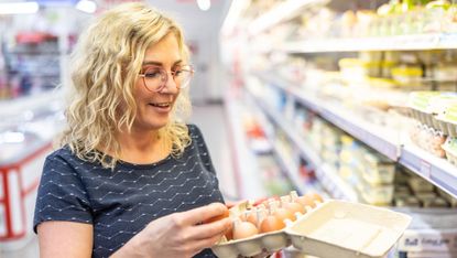 Woman looking at open carton of eggs in supermarket
