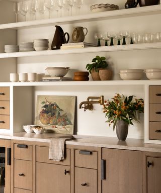 Kitchen shelves with glasses, rustic vases and plates and sink with gold tap, wooden cupboards and marble countertop