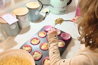 Child adding cupcake mixture into cupcake cases lined in a bun tray