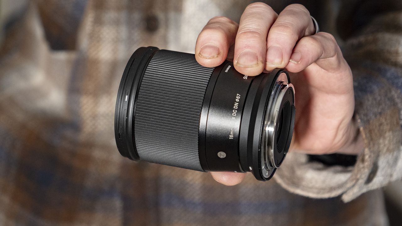 Sigma 16mm F1.4 DC DN Contemporary lens in the hand, checked shirt background