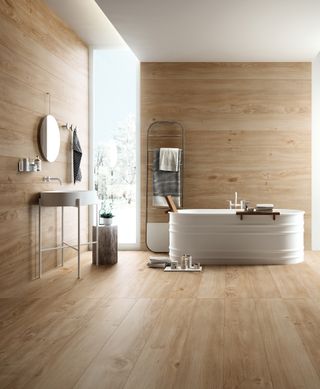 A large bathroom with wood effect porcelain tiles on the walls and floor with a white bath and white storage