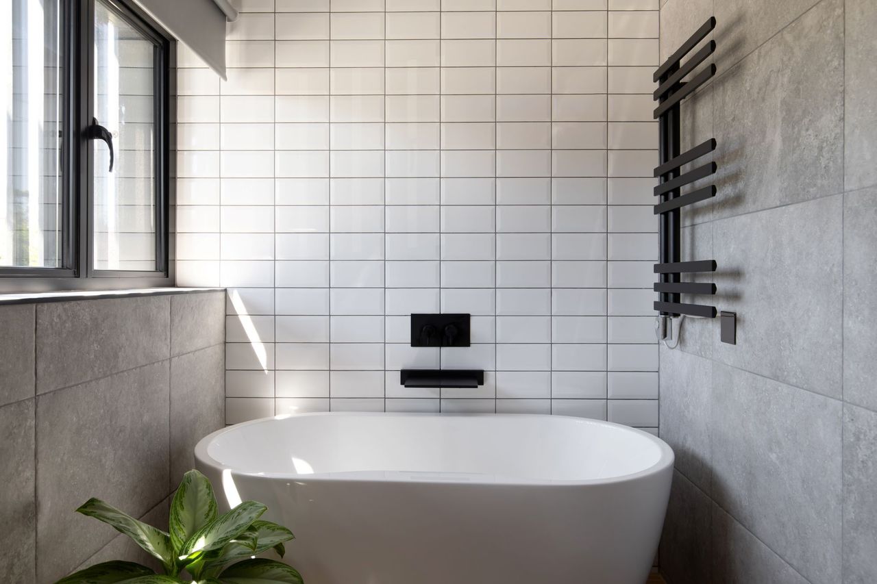 A white tiled bathroom with large bath and black taps