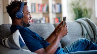 Gifting music streaming: man sitting on sofa and listening to music through his wireless headphones