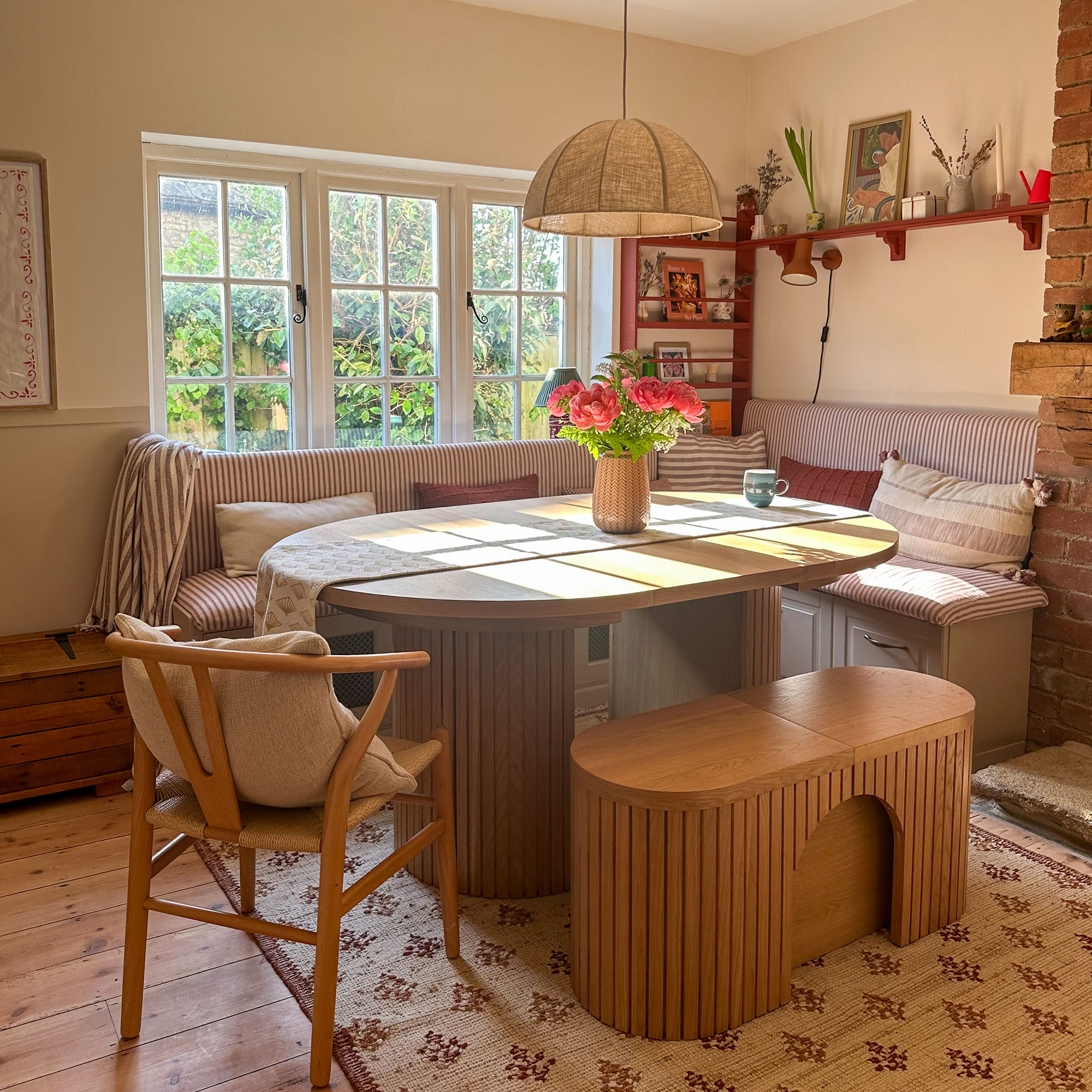 Corner kitchen banquette area with striped upholstery, around oval wooden table and topped with pendant lamp shade