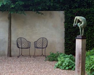 sculpture on a plinth next to a garden wall
