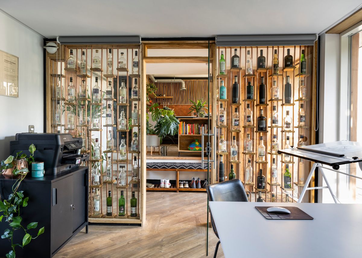 A home office with glass walls containing empty whiskey bottles of various shapes and sizes