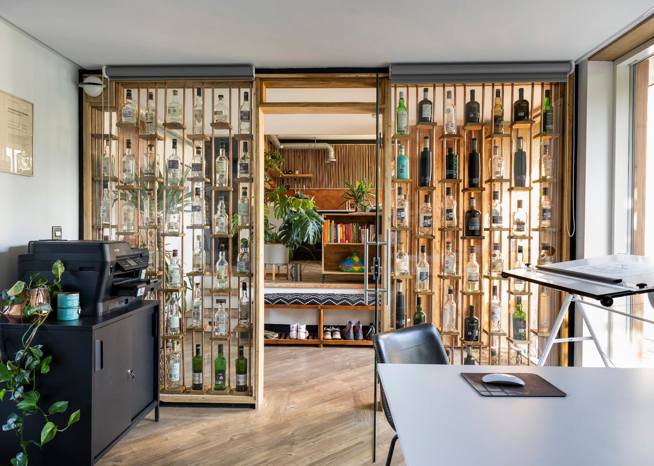 A home office with glass walls containing empty whiskey bottles of various shapes and sizes