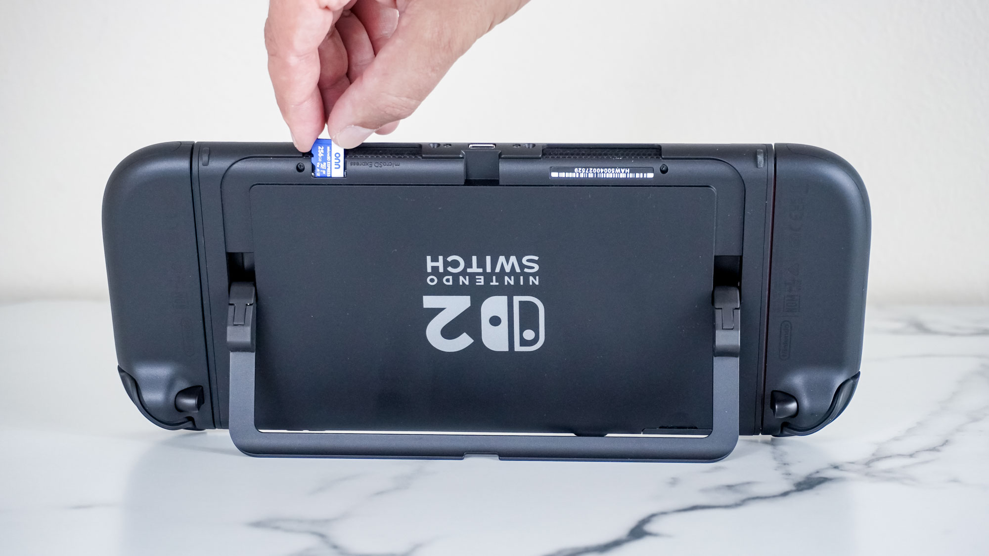 Inserting a microSD Express card into the Switch 2 with the console upside down on a desk