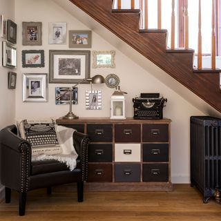 chest of drawers and gallery wall with armchair in space under the stairs