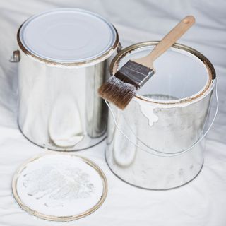 Two tins of white paint on a white dust sheet with a paintbrush laying on top