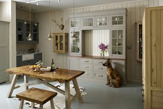 white kitchen with dresser and wooden farmhouse dining table and industrial lighting