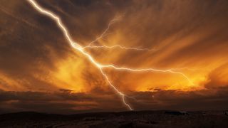 An image of lightning striking towards the ground during a thunderstorm at sunset.