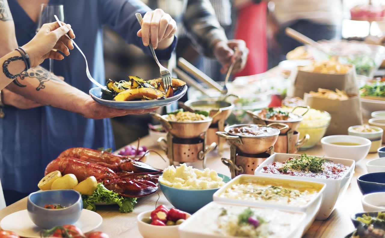 Buffet food spread with people scooping food onto plates