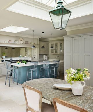 Kitchen layout ideas in a large traditional kitchen with pale cabinetry, a blue breakfast bar and wooden dining table.