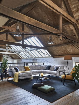 loft living room with vaulted ceiling, grey sectional on blue rug, armchairs, pendant lights