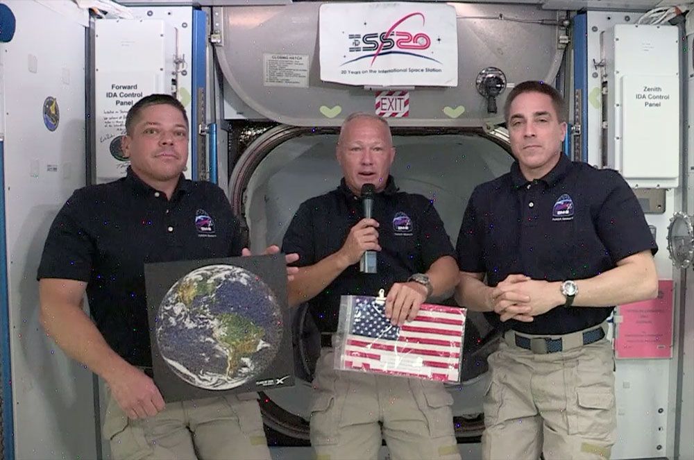 NASA astronaut and SpaceX Crew Dragon spacecraft commander Doug Hurley, flanked by his crewmate Bob Behnken and Expedition 63 commander Chris Cassidy, displays the U.S. flag &quot;captured&quot; by SpaceX as the first U.S. company to launch astronauts to the space station, on Monday, June 1, 2020.