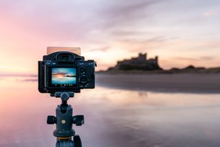 Camera on a tripod with square filters and colorful golden hour in scenic seascape