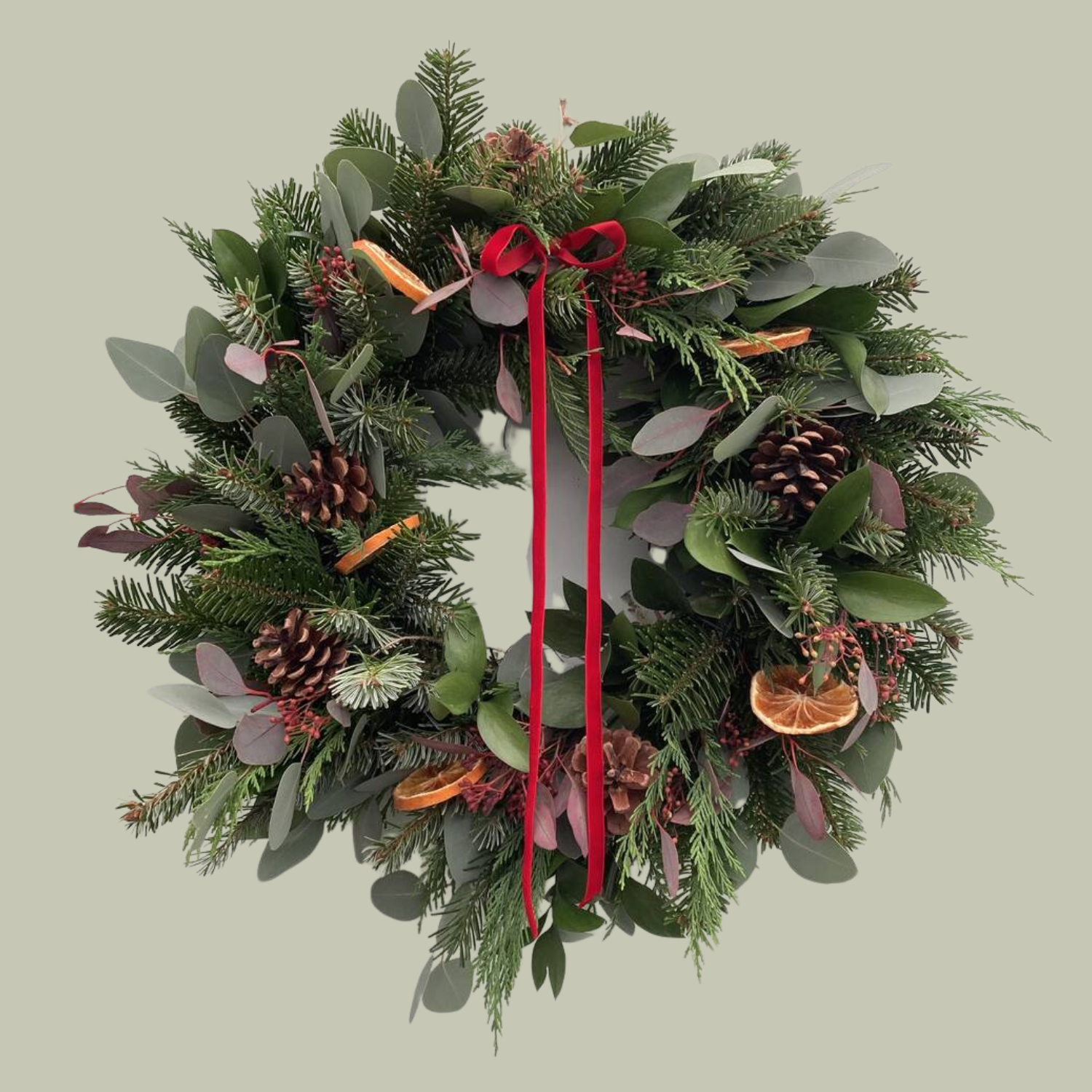 A Christmas wreath with fresh fir, dried oranges, pinecones, and a red ribbon
