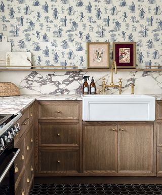 oak kitchen cabinets with marble splashback and grey and white toile de Jouy style wallpaper above