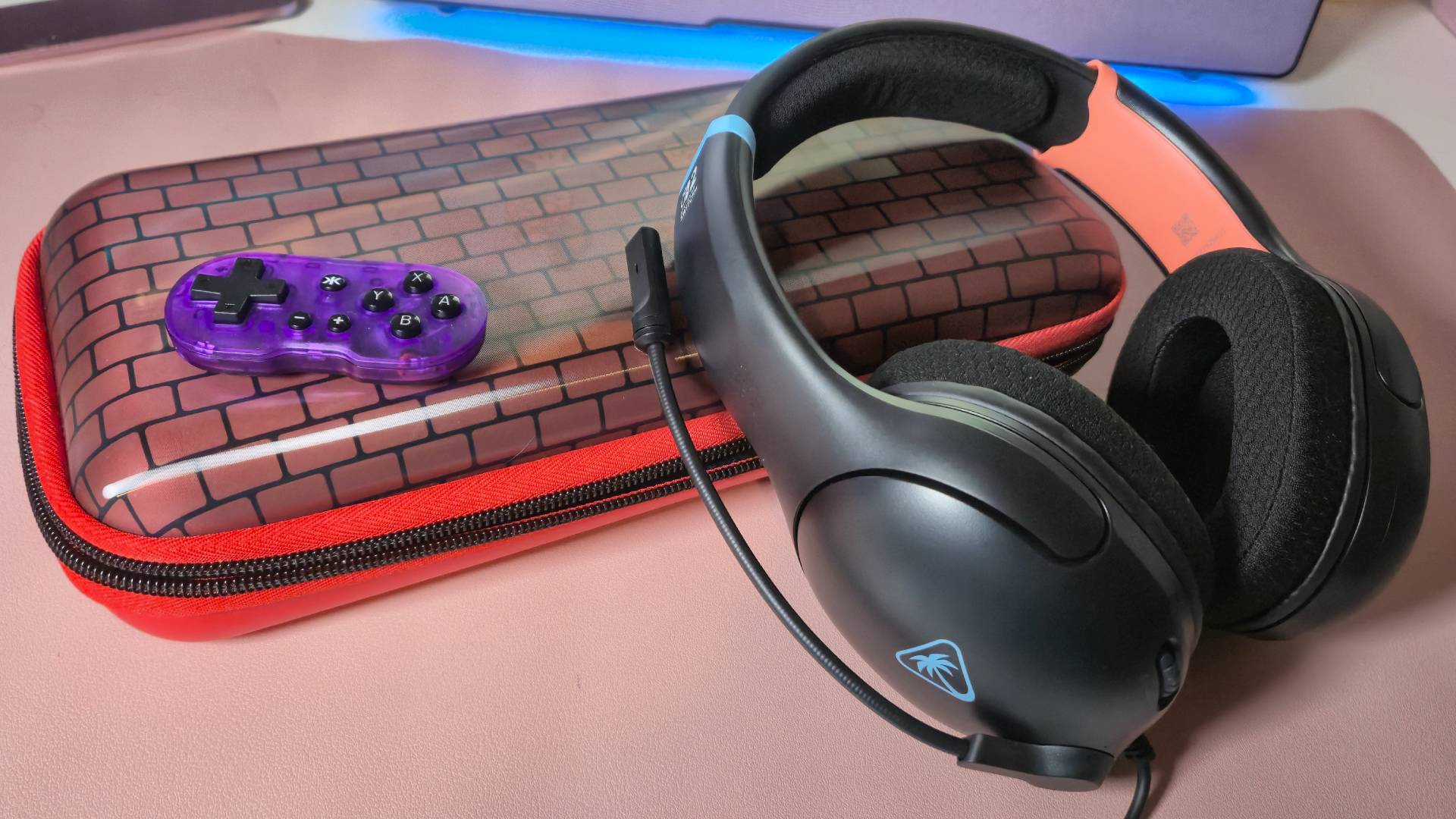 Photo of a black wired headset sitting on a Switch 2 case on a pink mouse pad.
