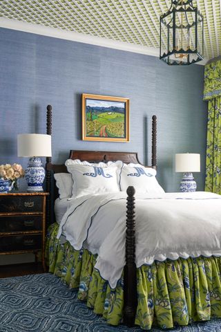 bedroom with traditional dark wood turned post bed and frilled bed skirt with frilled green floral curtain fabric and blue textured wallpaper