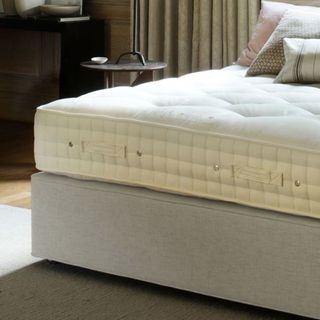 A corner of a mattress on a grey upholstered divan bed base in a bedroom