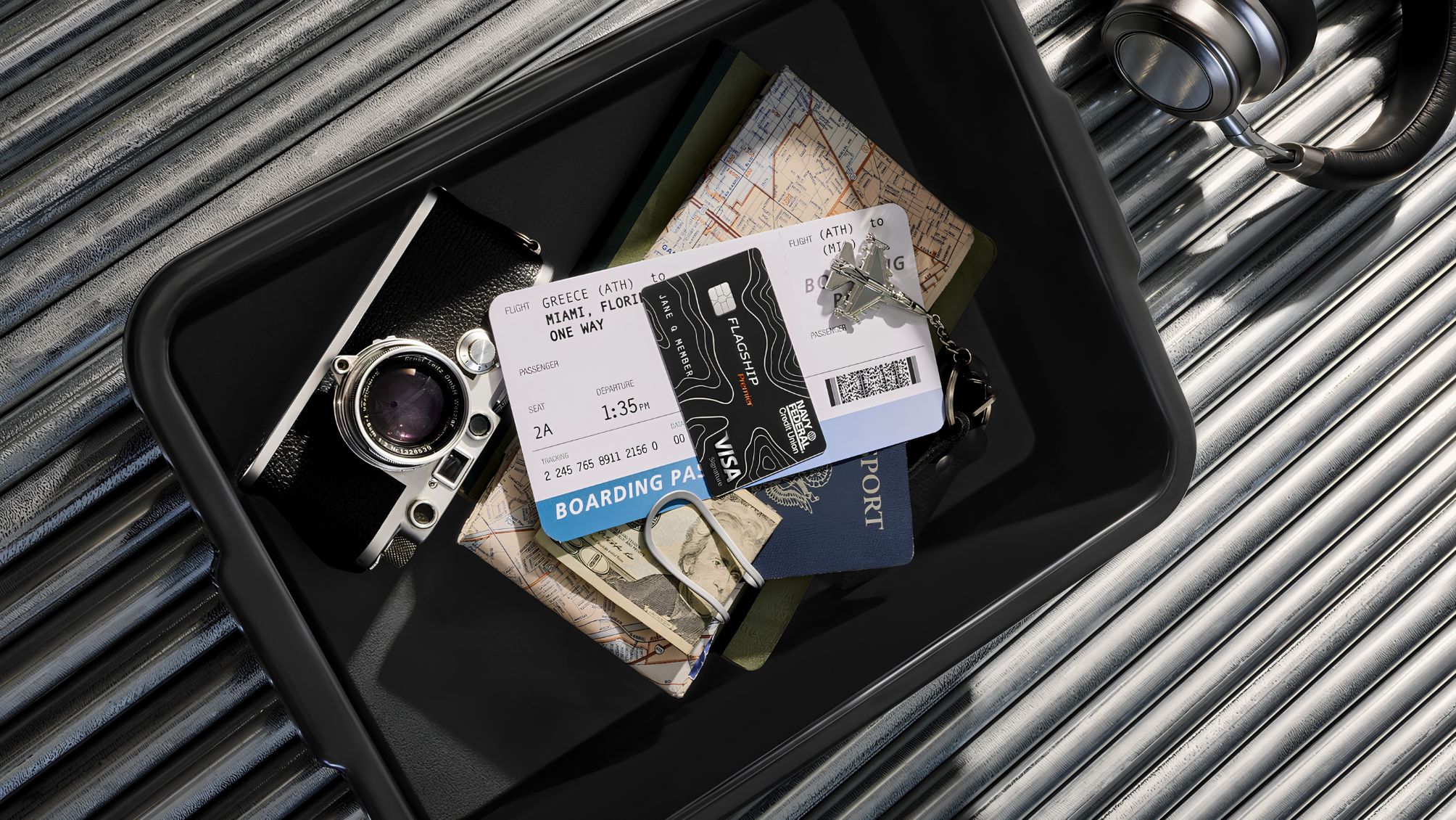 A TSA bin containing a camera, plane ticket, passport, and Navy Federal Visa card. 