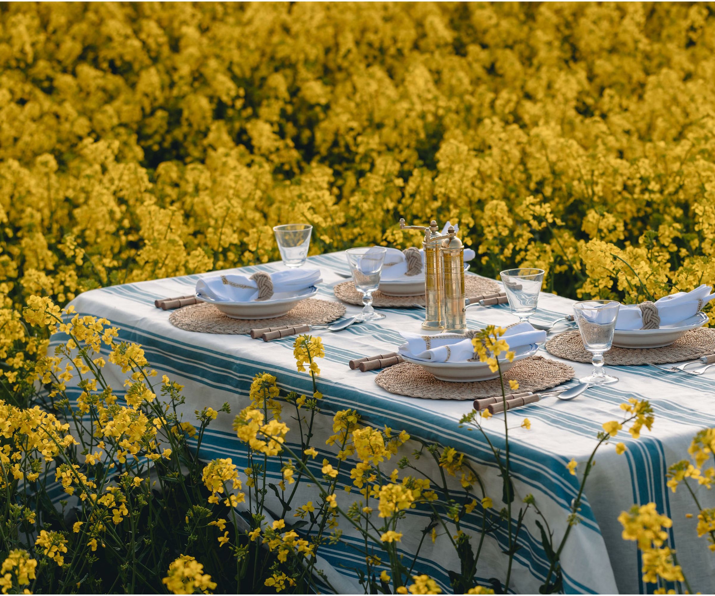 long table with a blue and white striped tablecloth, rattan round charger, bamboo flatware and white napkin