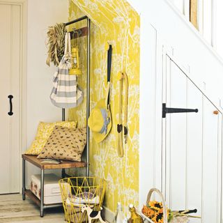 yellow wallpapered hallway with white cupboard under the stairs