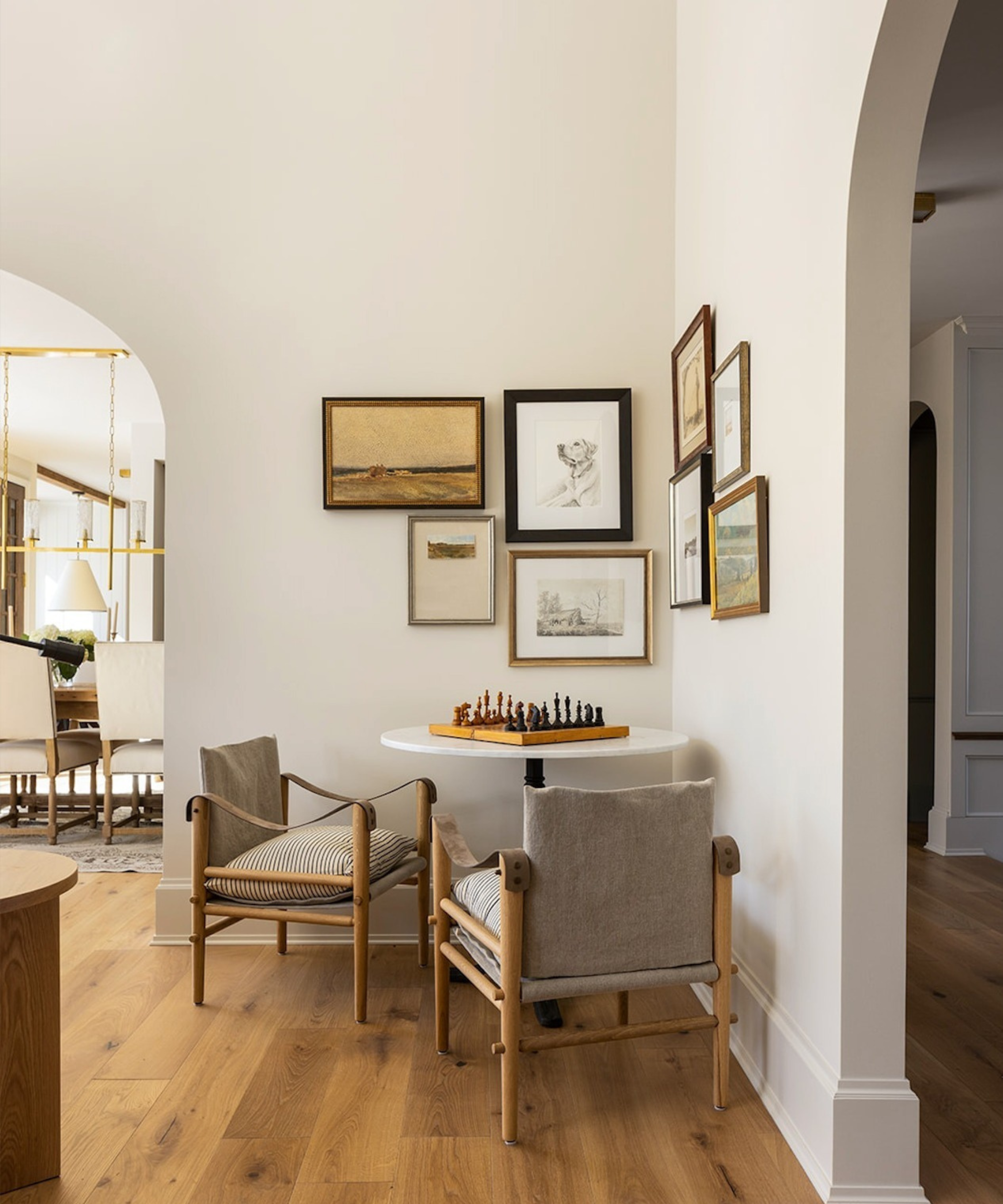 a seating area with two chairs, a table, a chess board, and a cluster of pictures framed on the wall above