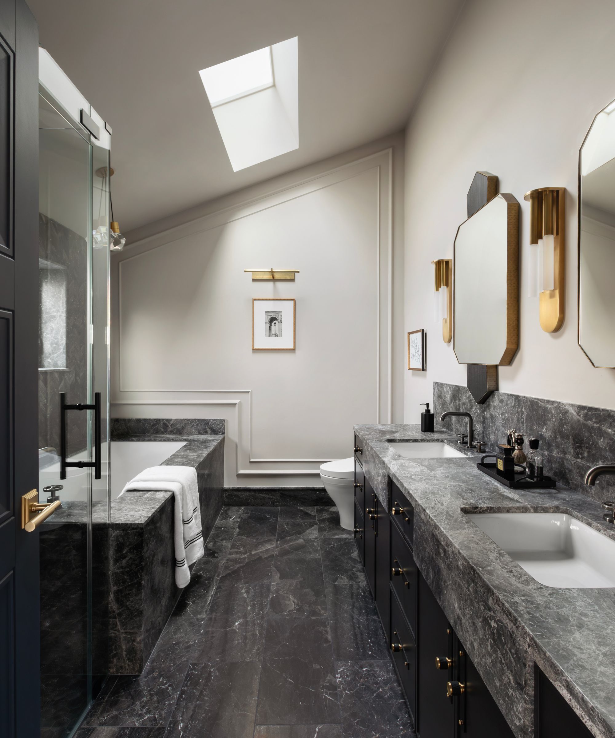 Sophisticated bathroom with a dark marble-clad tub and double vanity, black cabinetry, and a skylight illuminating the sloped ceiling.