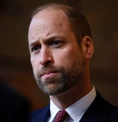 A headshot of Prince William wearing a white shirt and red tie looking serious