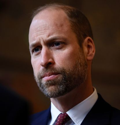 A headshot of Prince William wearing a white shirt and red tie looking serious