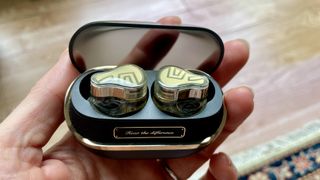 SoundPeats H3 earbuds and case held in a hand, in a living room