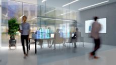 An office meeting room with glass walls, with blurred figures walking past