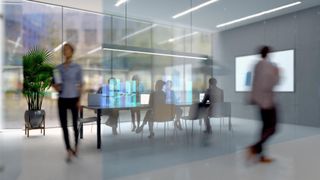 An office meeting room with glass walls, with blurred figures walking past