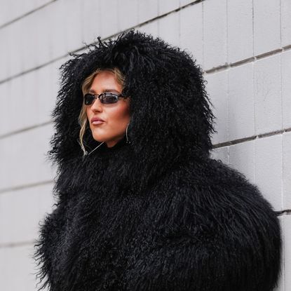 Emili Sindlev wears black faux fur shearling hooded Michael Kors mongolian coat, shiny black knee high heeled boots leather shoes, outside Michael Kors, during the New York Fashion week Fall/Winter 2025 on February 11, 2025 in New York, New York