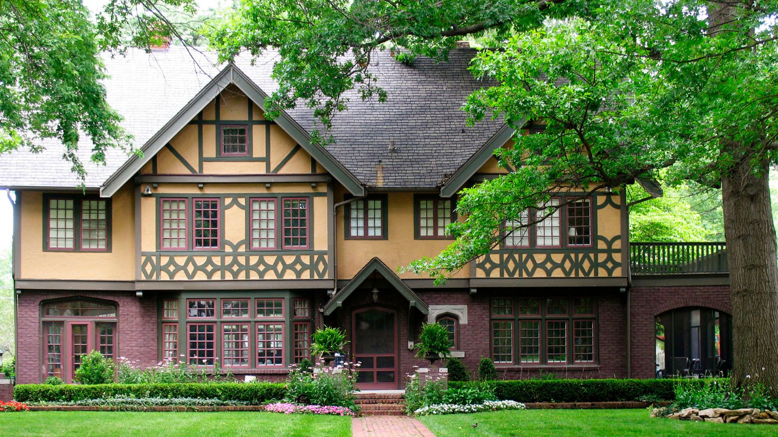 Tudor revival style house painted yellow and red with large tree and lawn