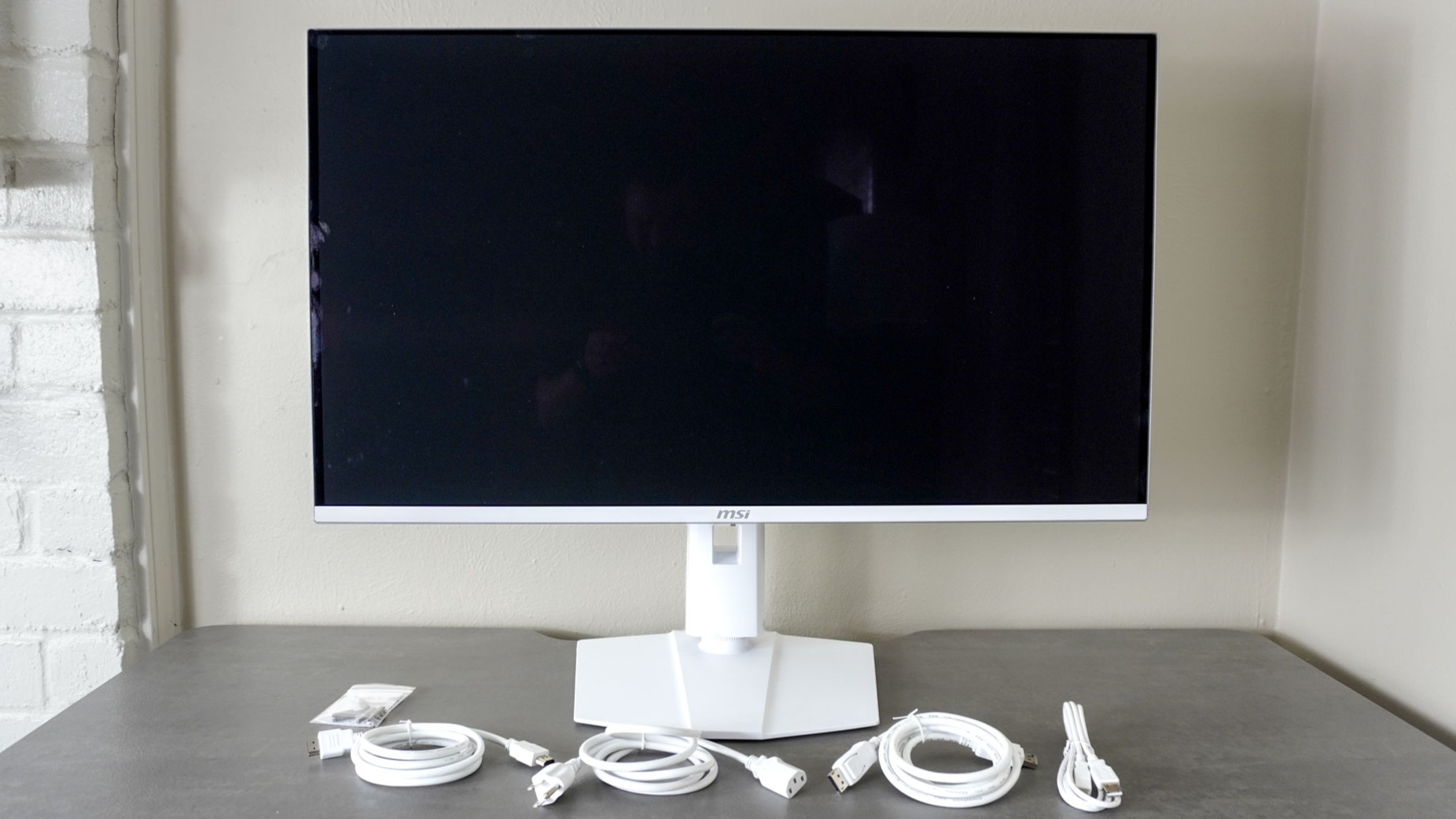 The MSI MPG 321URXW QD-OLED monitor on a desk with all of the included cables and accessories