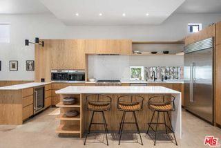 A kitchen with light wooden cabinetry, a white quartz island countertop, and grey walls