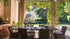 a pergola covered outdoor dining area with rattan chairs and table laid for breakfast