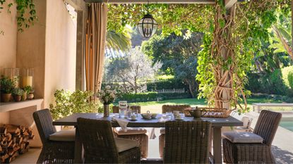 a pergola covered outdoor dining area with rattan chairs and table laid for breakfast