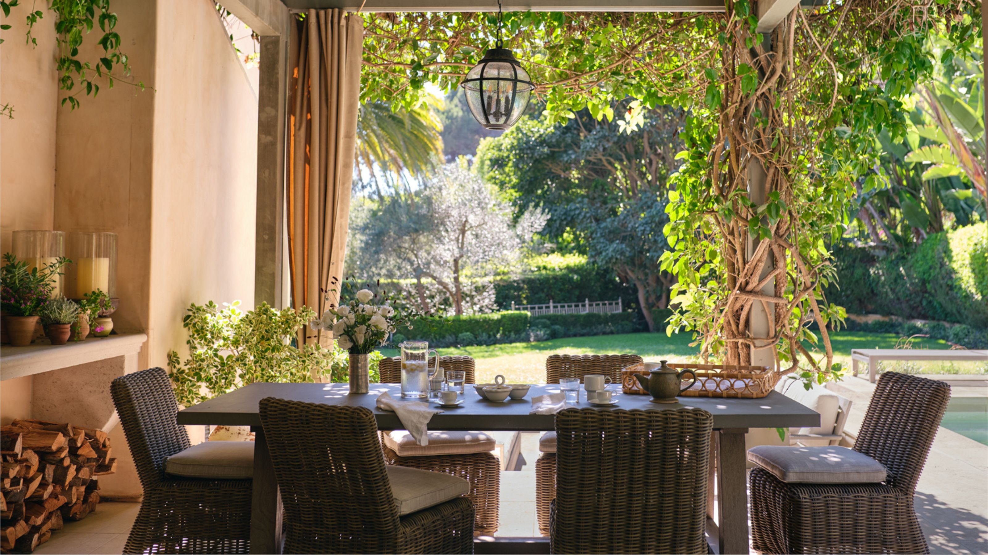 a pergola covered outdoor dining area with rattan chairs and table laid for breakfast