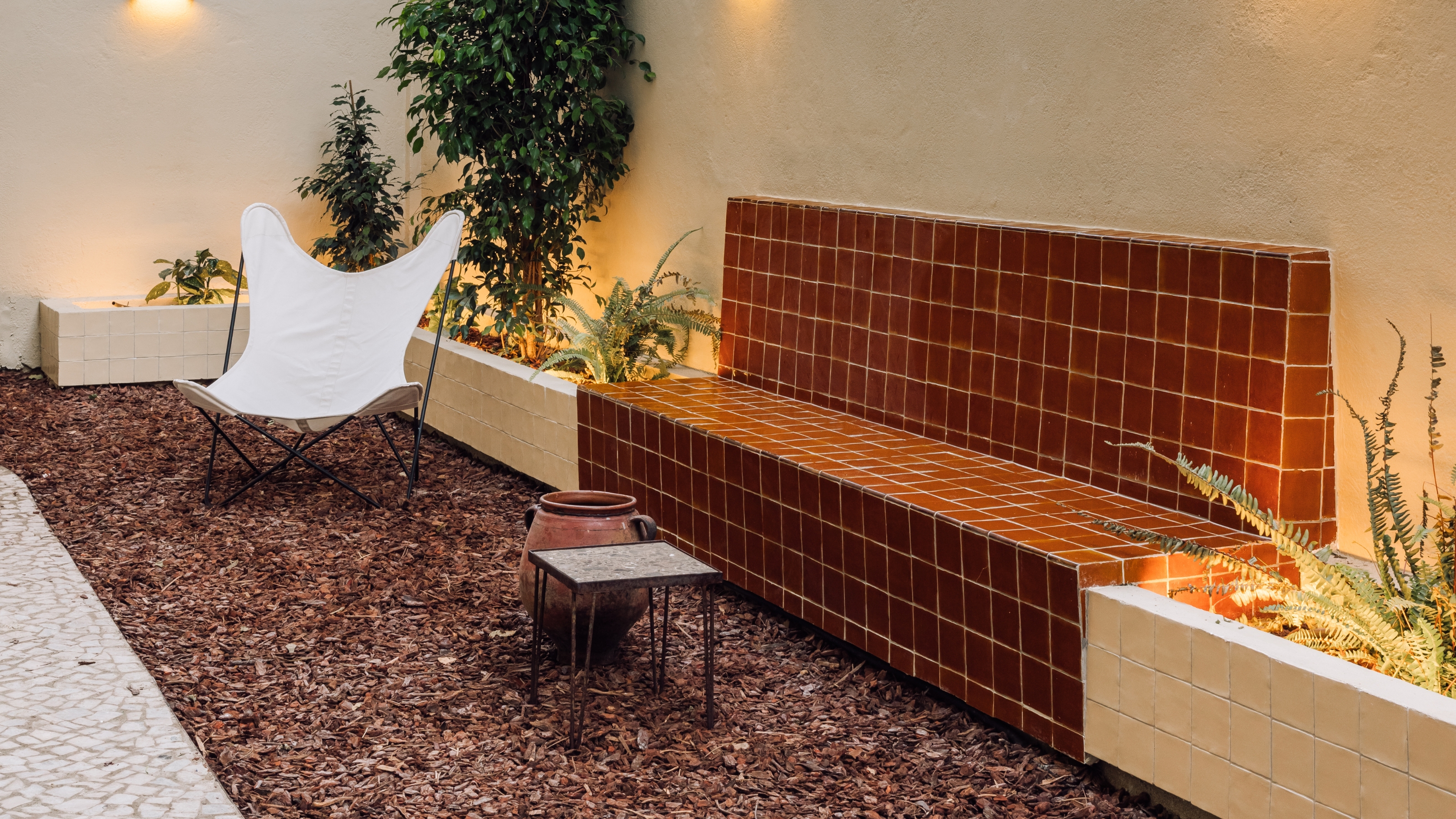a small woodchip garden with a tiled, rust colored outdoor bench