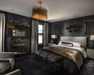 A black bedroom with gray-black walls, a gold light fitting and velvet throws