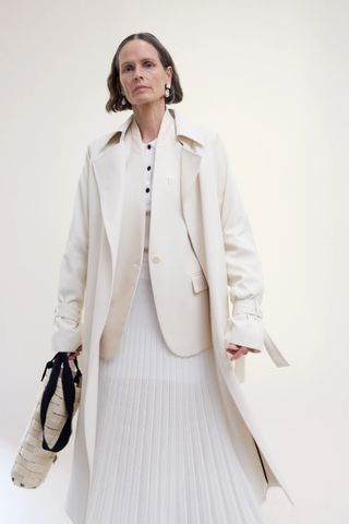 A woman wearing a white dress, blazer, and jacket by Maria McManus.