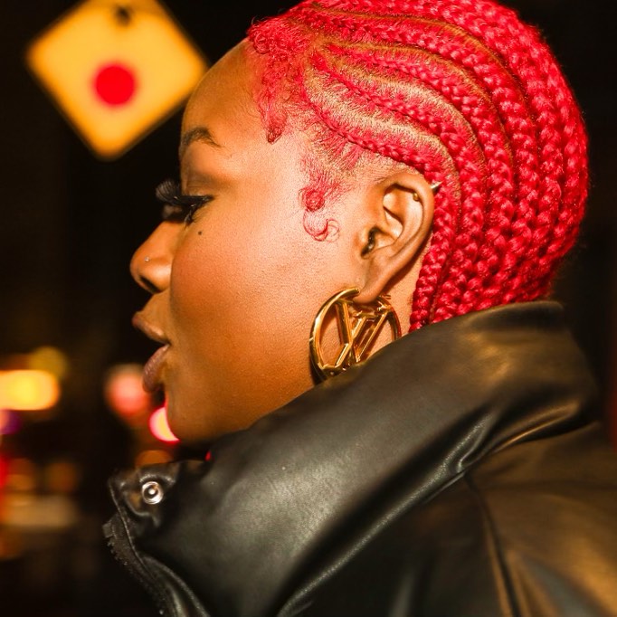 Side profile of a Black woman wearing a black puffer jacket with bright red colored braids.